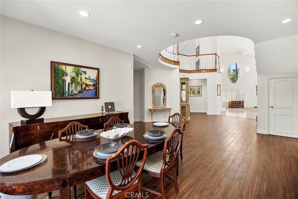 Dining room with a dark wood table, hardwood floors, and a curved staircase in the foyer.
