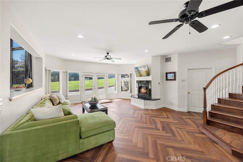 Living room with a green sectional, herringbone wood floors, corner fireplace, and curved staircase.
