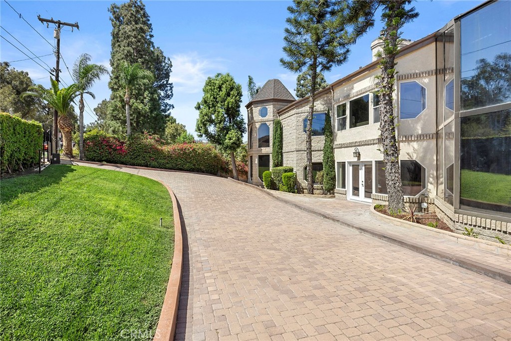 Large stone-and-stucco home with a turret beside a curved brick-paver driveway and manicured lawn.