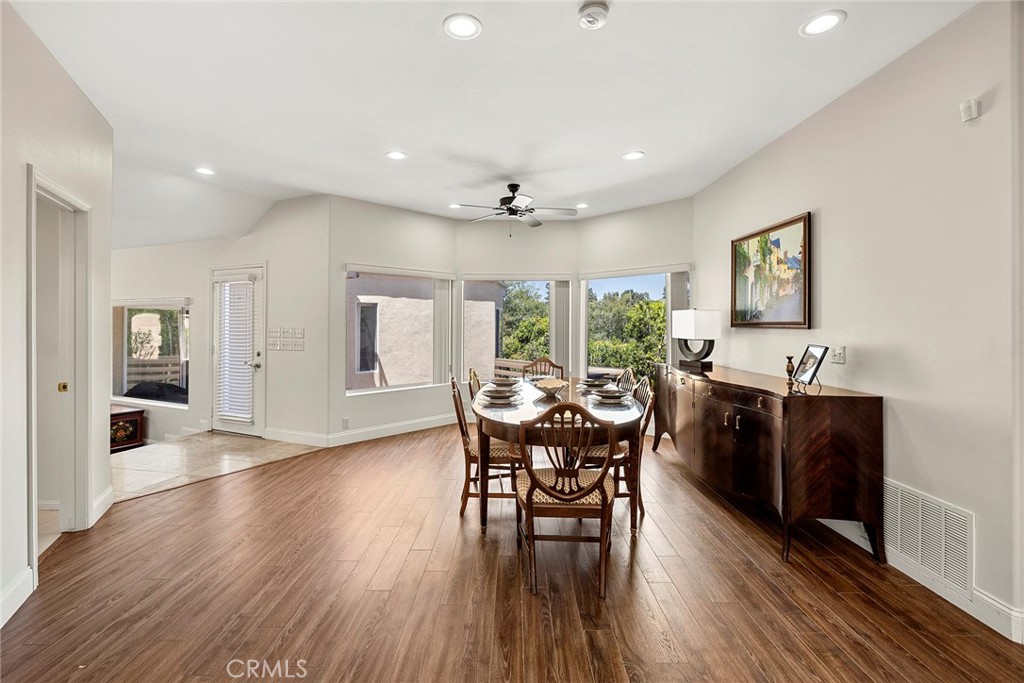Dining room with a long wooden table, dark sideboard, and large windows overlooking greenery.