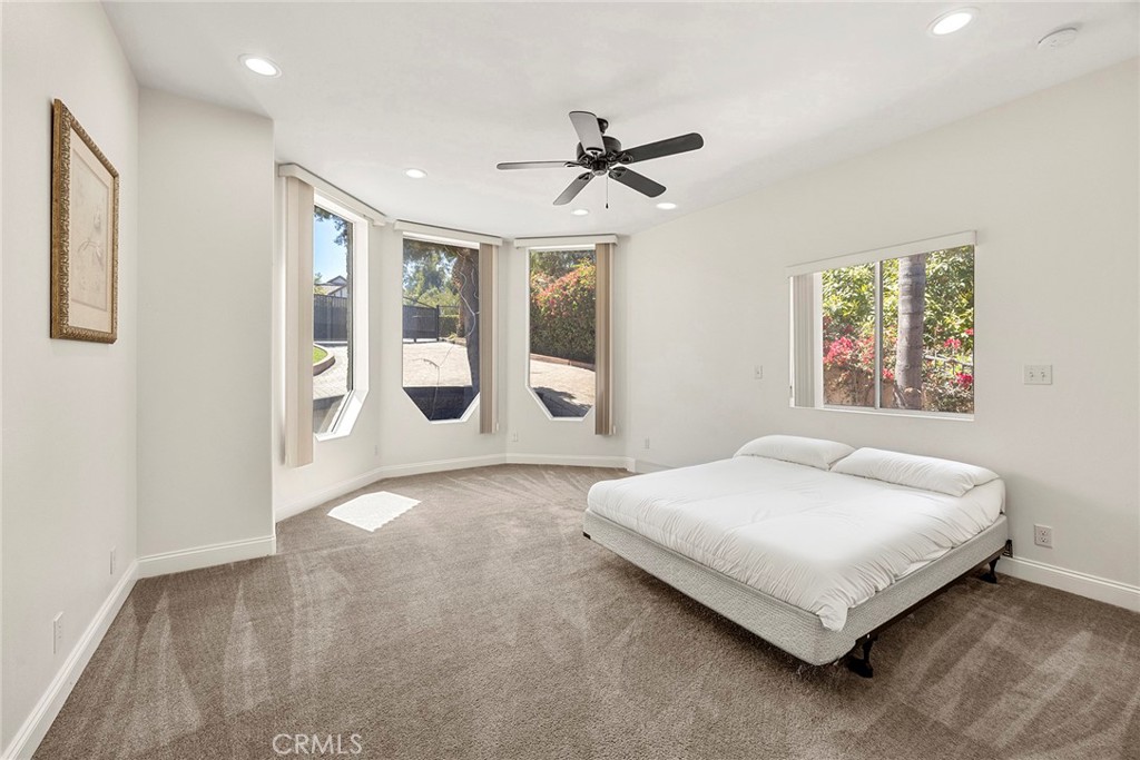 Bedroom with a low white bed and tall angled windows overlooking the yard.