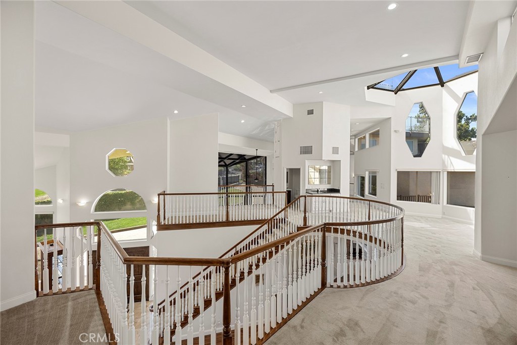 Spacious upstairs landing with a curved staircase, white balusters, vaulted ceiling, and geometric windows.