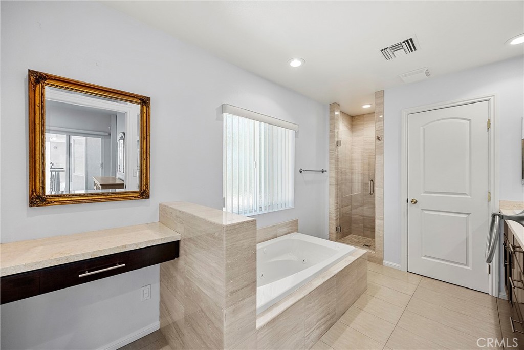 Bathroom with a built-in soaking tub, glass shower, and ornate gold-framed mirror.