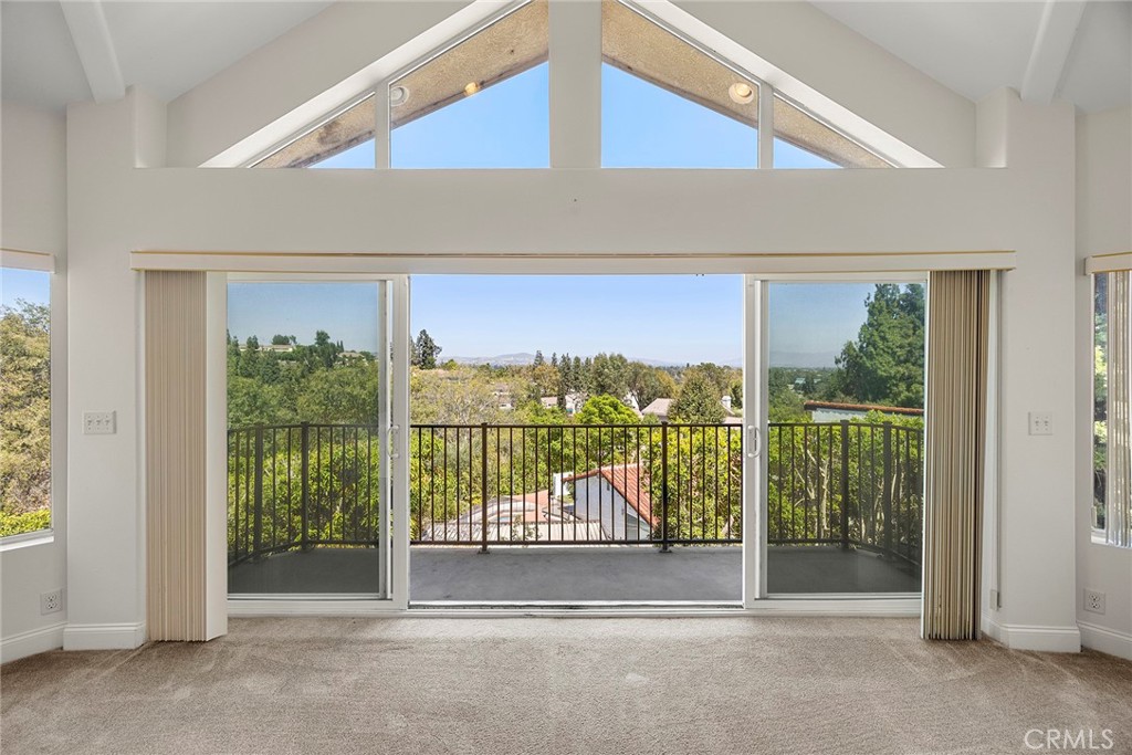 Vacant living room with vaulted windows, sliding doors, and a balcony overlooking trees.