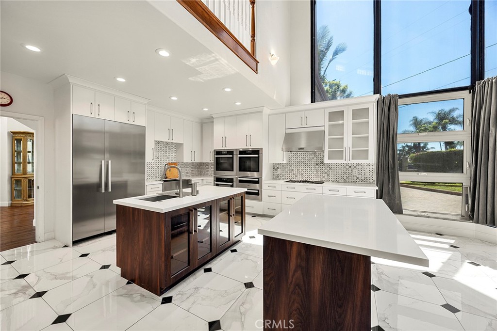 Bright modern kitchen with two islands, white cabinetry, marble-look tile, and tall windows.