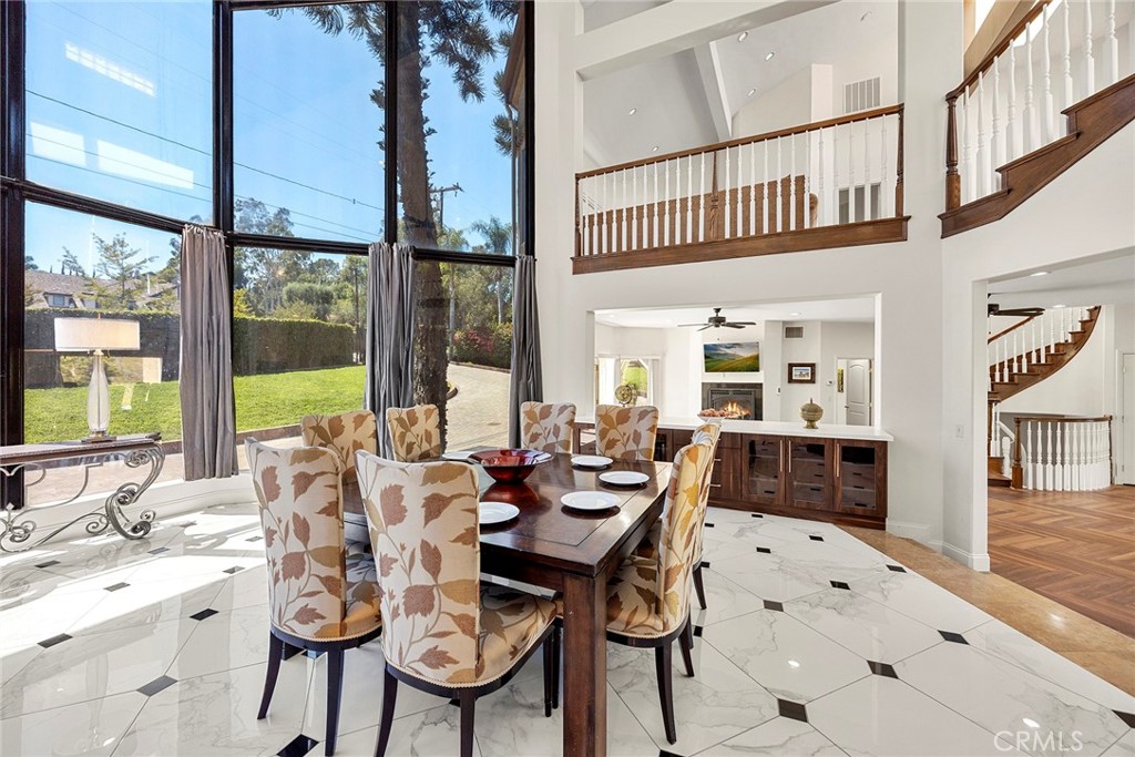 Formal dining room with tall windows, marble-pattern tile, and an open wooden staircase.