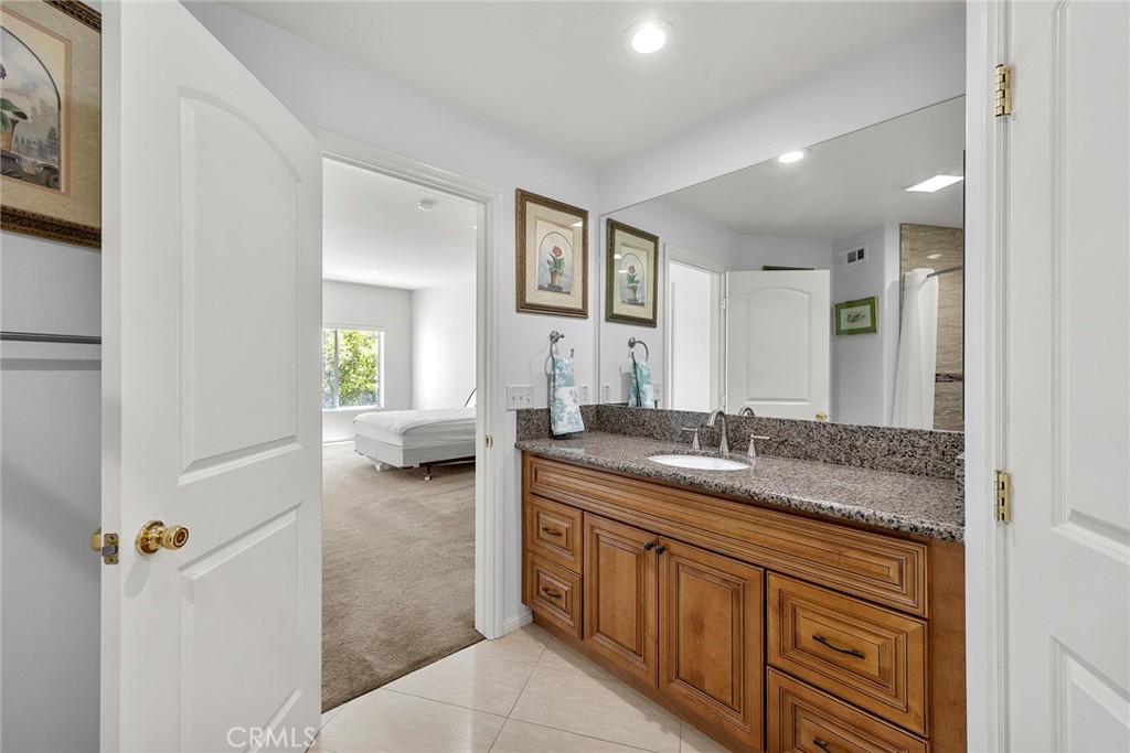 Bathroom vanity with granite counter and wood cabinets, opening onto a carpeted bedroom.