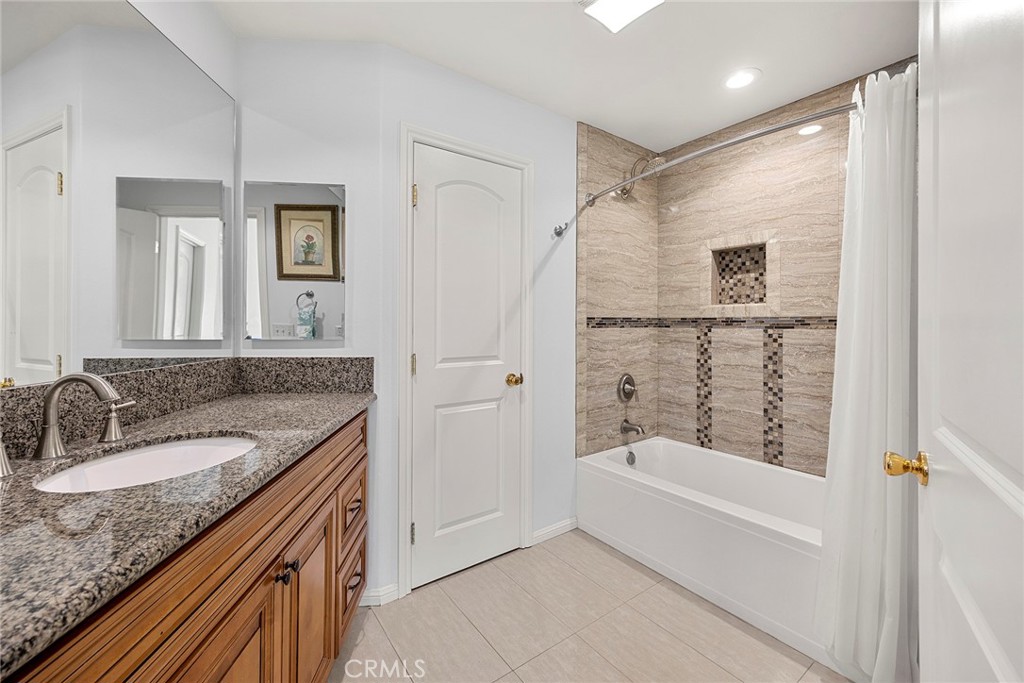 Bathroom with granite vanity and tiled tub-shower with mosaic accents.