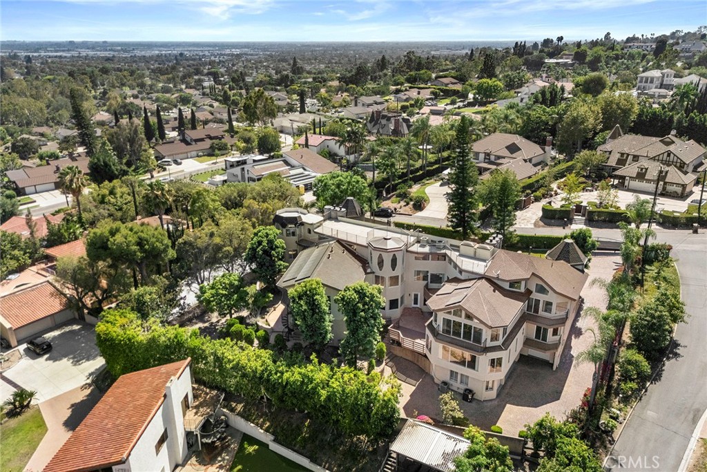 Large multi-story home with tan roofs and landscaped grounds, seen above a leafy residential neighborhood.