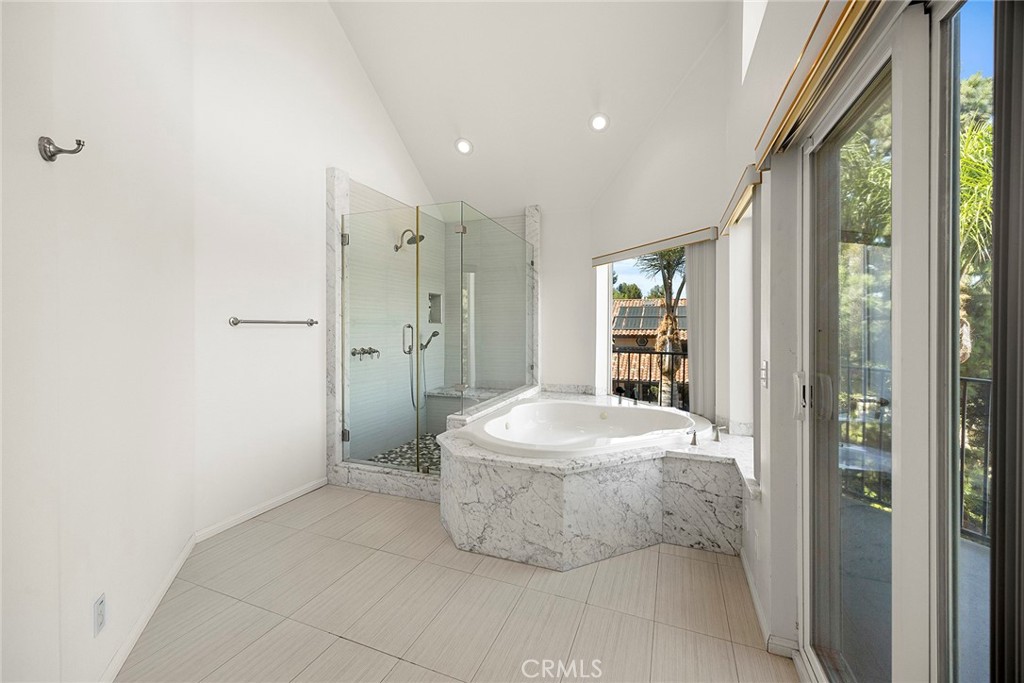 Bright bathroom with a marble-clad soaking tub, glass shower, and sliding doors to a balcony.