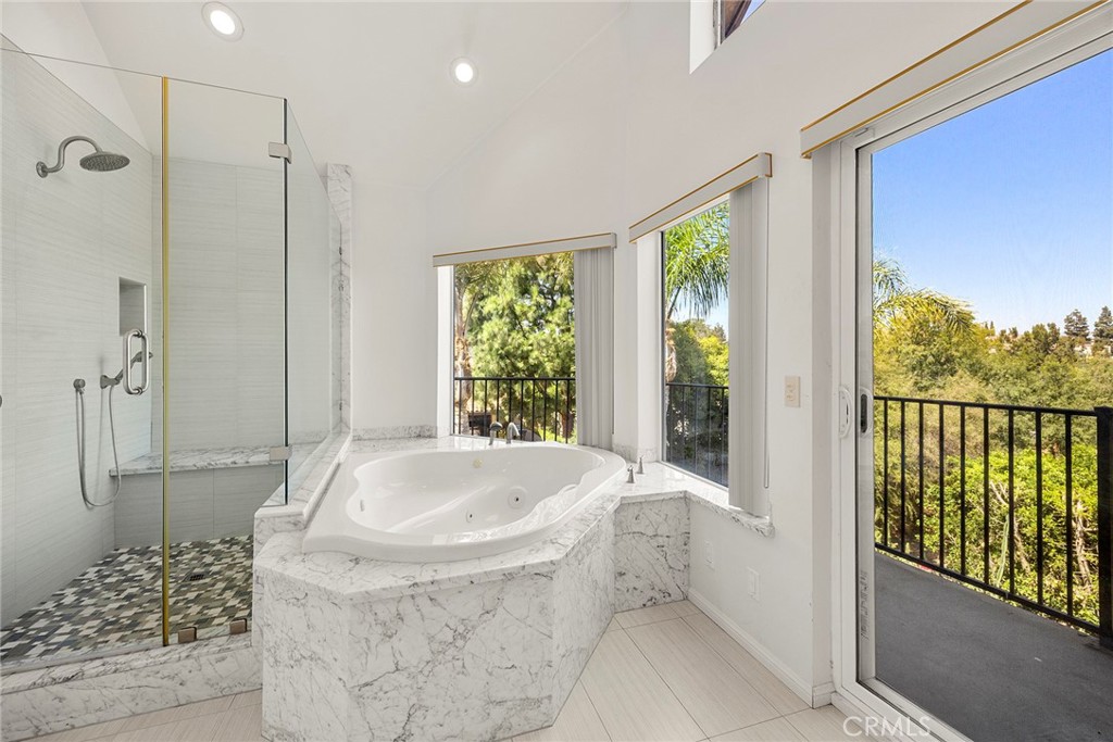 Bathroom with a marble-clad jetted tub, glass shower, and windows overlooking trees.