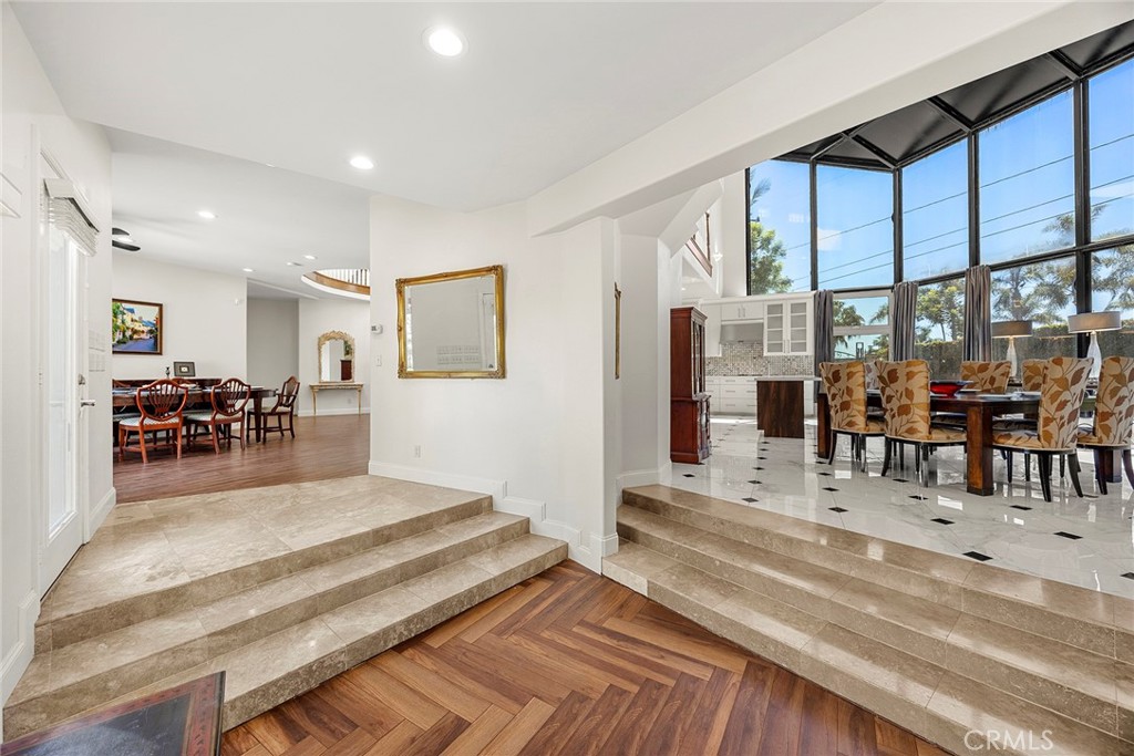 Split-level entry foyer with stone steps, patterned hardwood flooring, and tall windows beside the dining area.