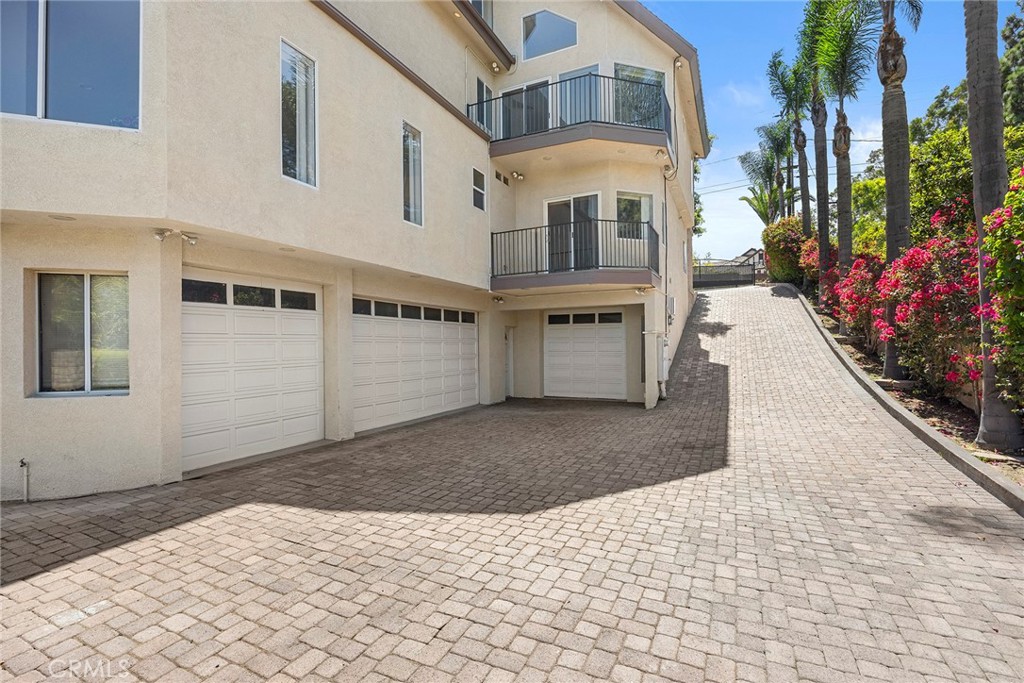 Home exterior with three garage doors, a brick-paver driveway, balconies, and palm landscaping.