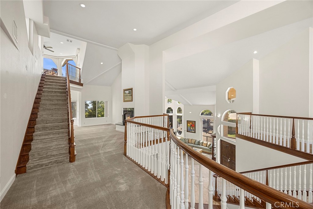 Upper-level foyer with a carpeted staircase and wood-railed landing overlooking a bright living room.