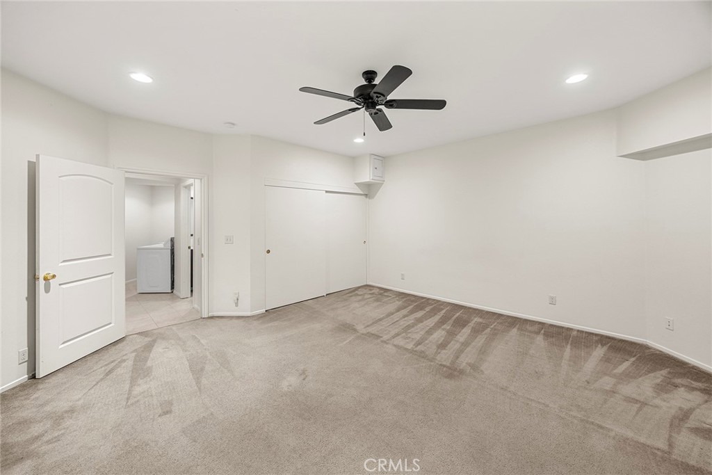 Empty carpeted room with a ceiling fan, sliding closet doors, and doorway to a laundry area.
