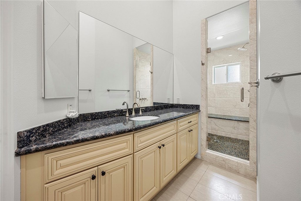 Bathroom with a cream vanity, dark granite countertop, and tiled walk-in shower.