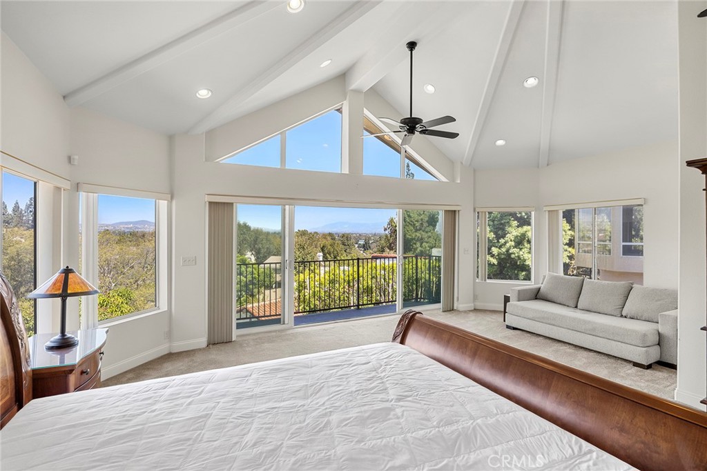 Bedroom with a vaulted ceiling, sitting area, and sliding doors opening to a balcony.