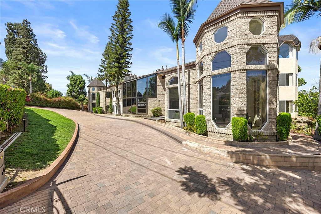 Stone residence with a tower and tall windows beside a curved brick-paved driveway.