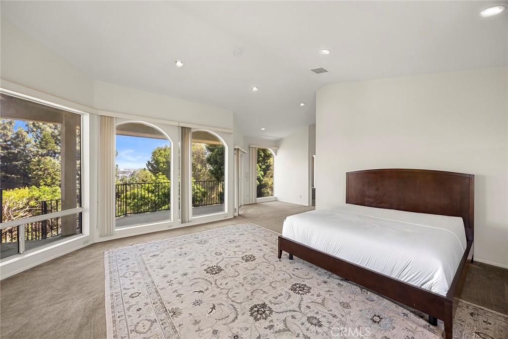 Spacious bedroom with arched windows, a dark wood bed, and a balcony overlooking trees.