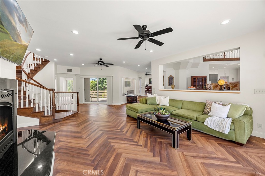 Living room with a green sectional, herringbone wood floors, fireplace, and curved staircase.