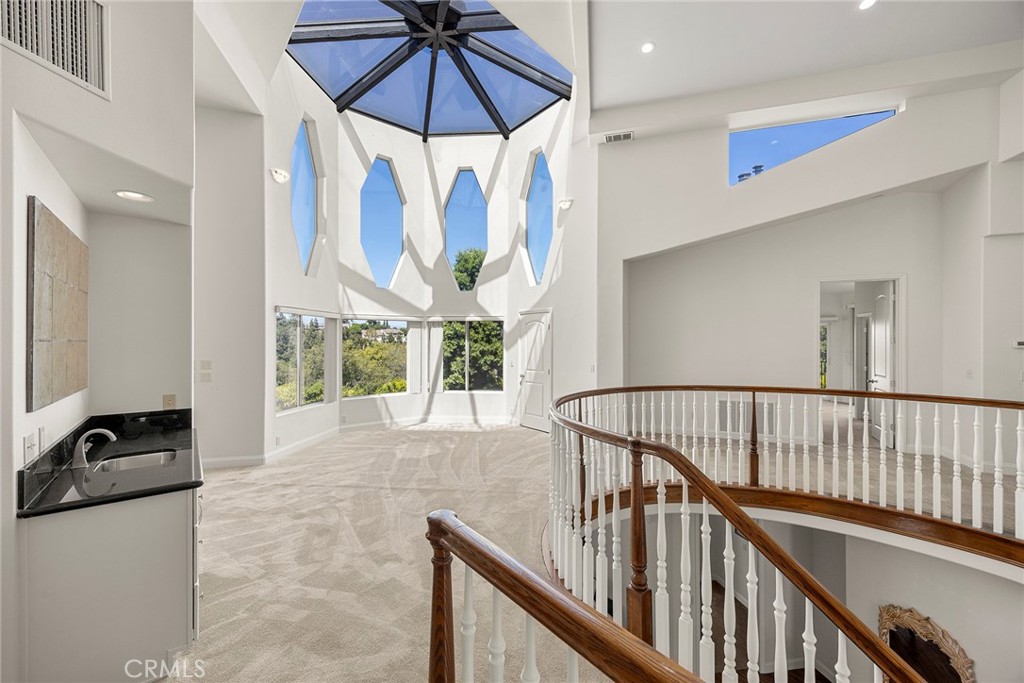 Open upstairs landing with a curved staircase railing beneath a geometric glass skylight.