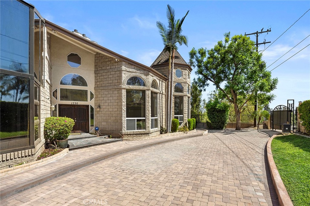 Stone-fronted home with arched windows and a turret beside a broad paver driveway.