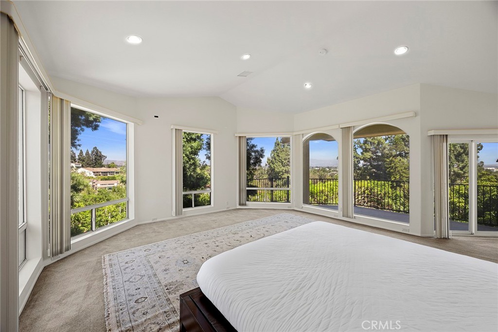 Bright bedroom with tall windows, balcony railing, and leafy neighborhood views.