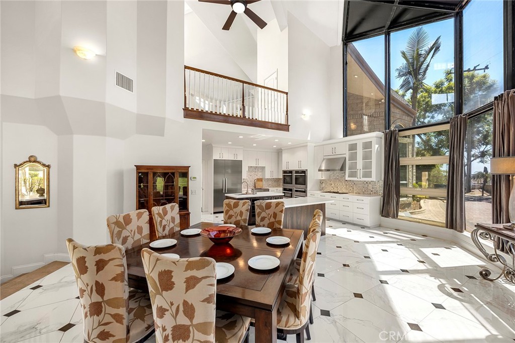 Dining area and kitchen beneath a vaulted ceiling, with large windows and marble-pattern floors.