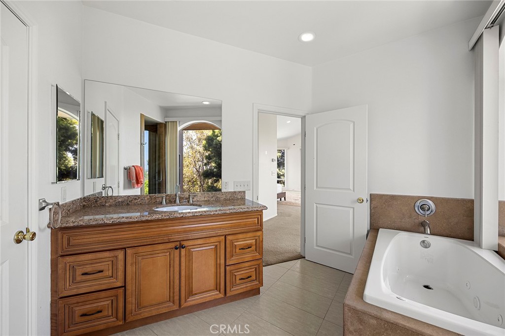 Bathroom with a wooden vanity, stone countertop, and built-in soaking tub.