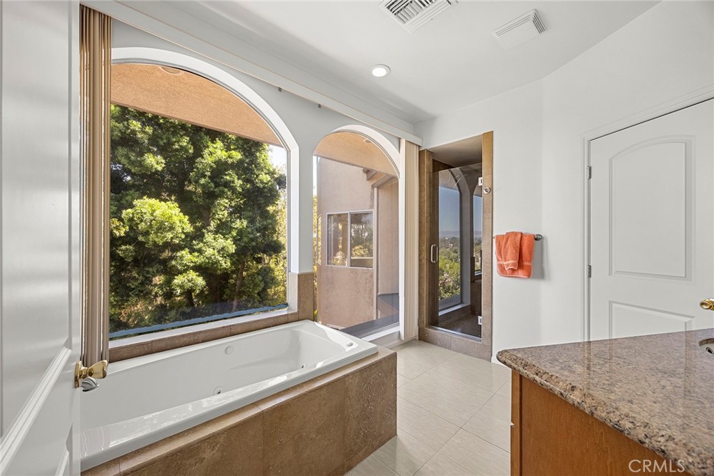 Bathroom with a built-in soaking tub beneath arched windows overlooking leafy trees.