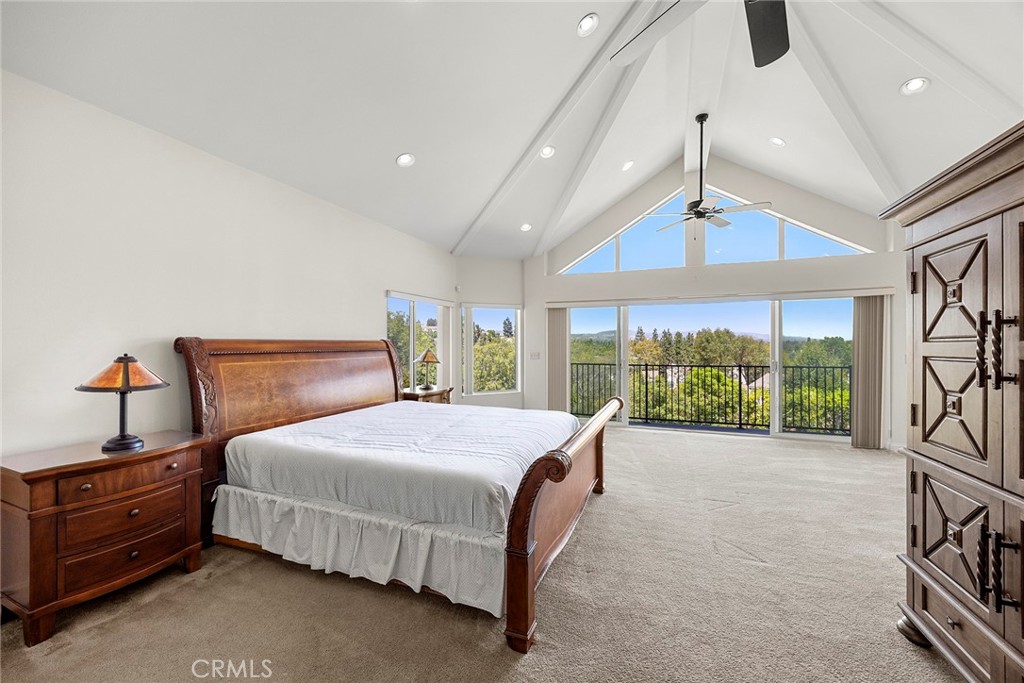 Furnished bedroom with vaulted ceiling, balcony, and views of tree-covered hills.