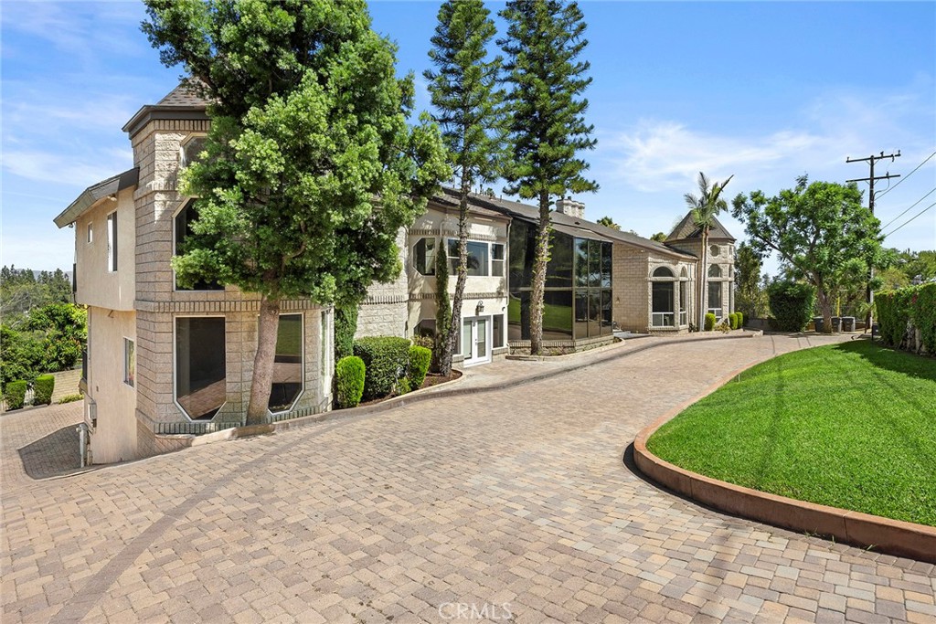 Large stone-and-stucco home beside a broad brick-paved driveway and curved lawn.