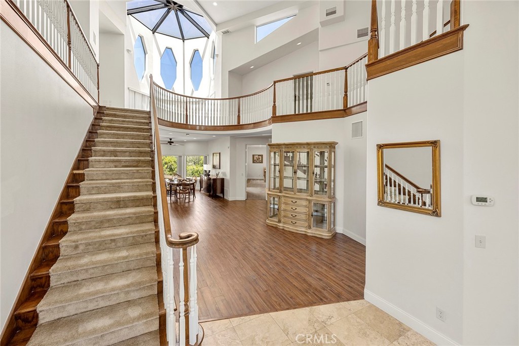 Two-story foyer with a sweeping staircase, curved balcony, skylight, and wood flooring.