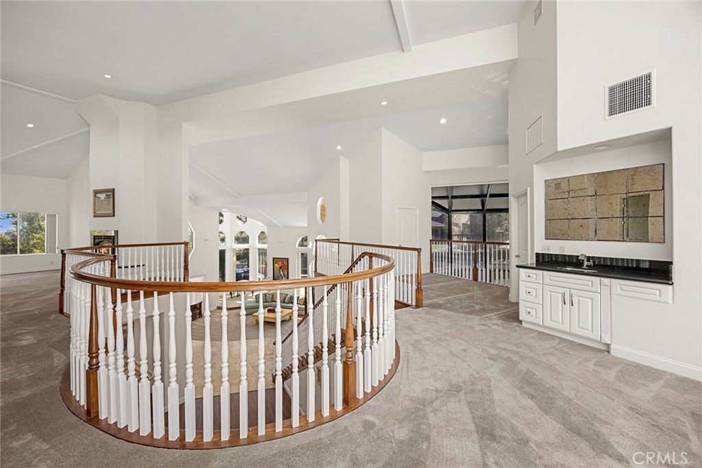 Upper-level landing with a curved wood-and-white railing, gray carpet, and built-in cabinet.