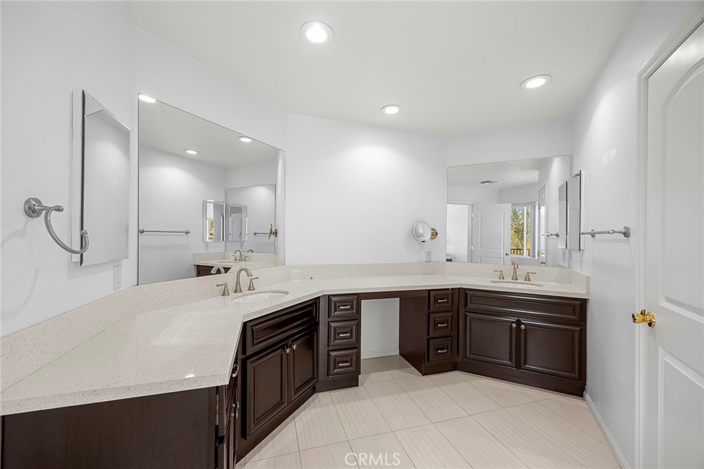 Bathroom with an L-shaped double-sink vanity, dark wood cabinetry, and expansive mirrors.