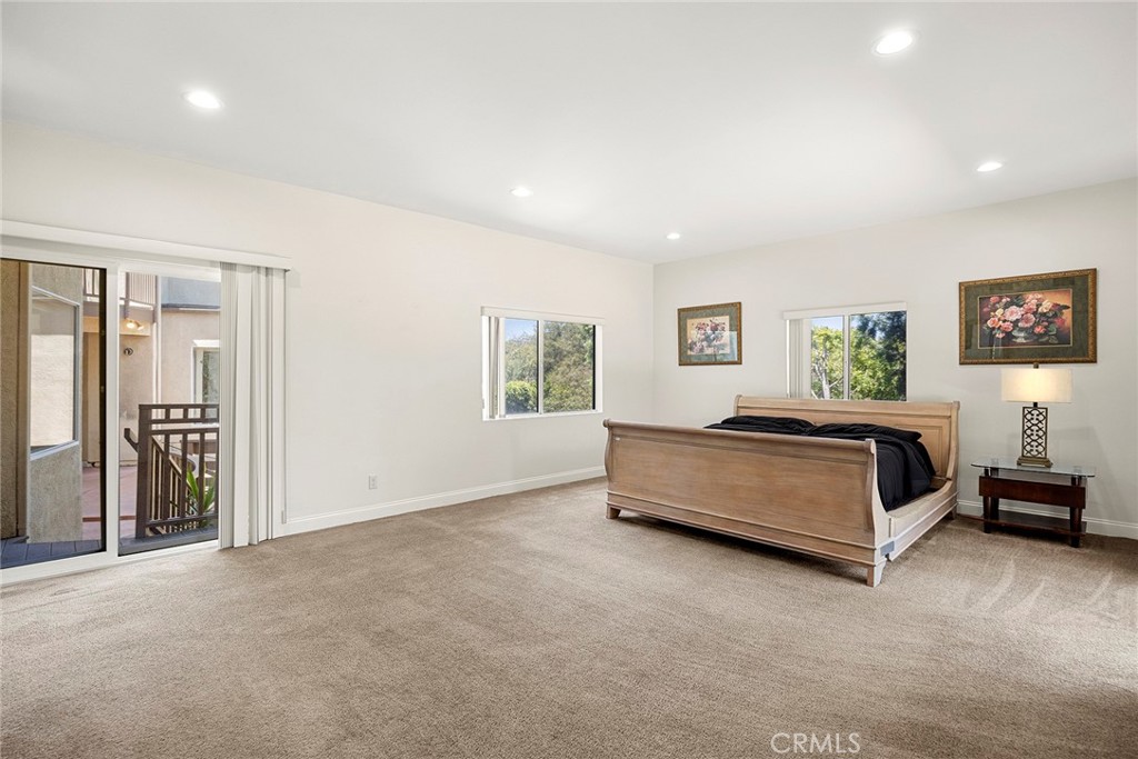Primary bedroom with a wooden bed, beige carpet, and sliding glass doors to a balcony.