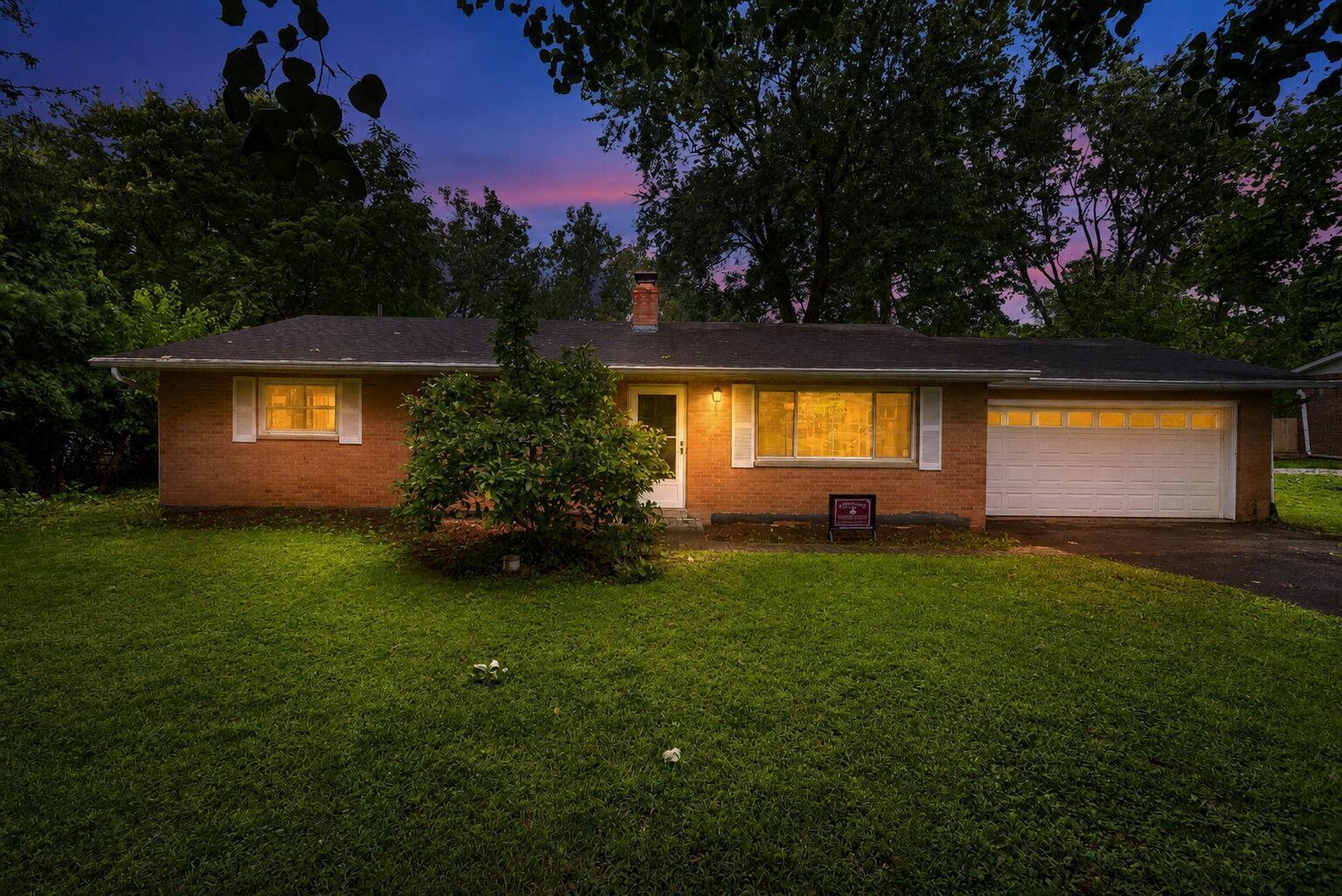 Single-story brick home with an attached garage and glowing windows at dusk.