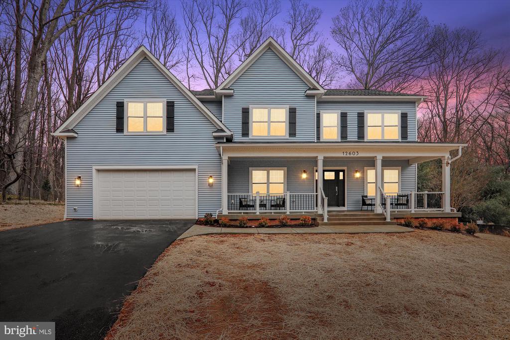 Blue-gray two-story house with a two-car garage and covered front porch at dusk.