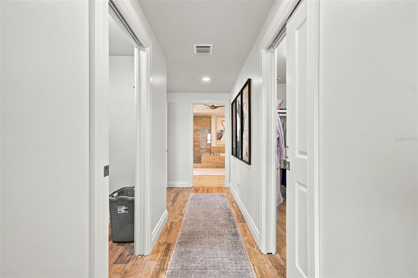 White hallway with warm wood floors, a gray runner, and a tiled bathroom at the far end.