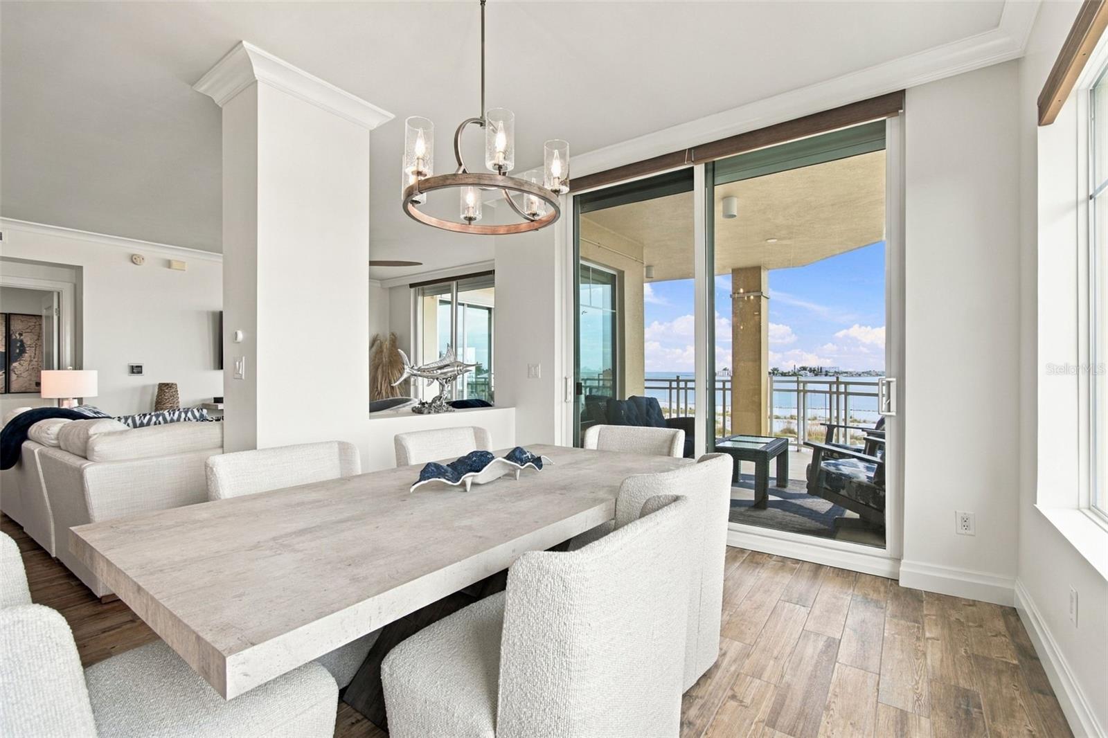 Dining area with a large stone table and balcony doors overlooking the water.