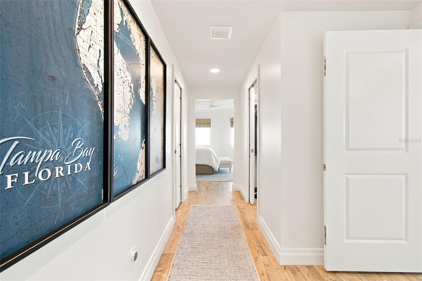 Hallway with framed Tampa Bay maps, wood flooring, and a runner leading to a bedroom.