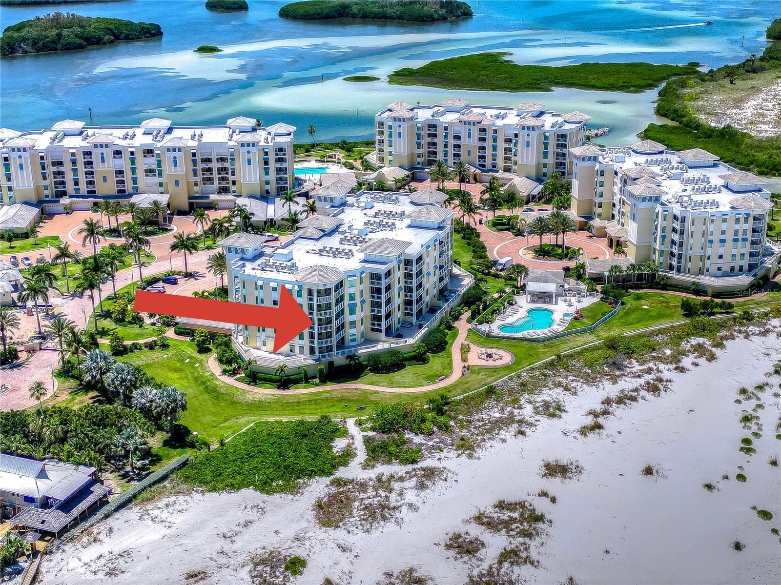 Aerial view of beachfront condominium complex, with an arrow marking one building beside the pool.