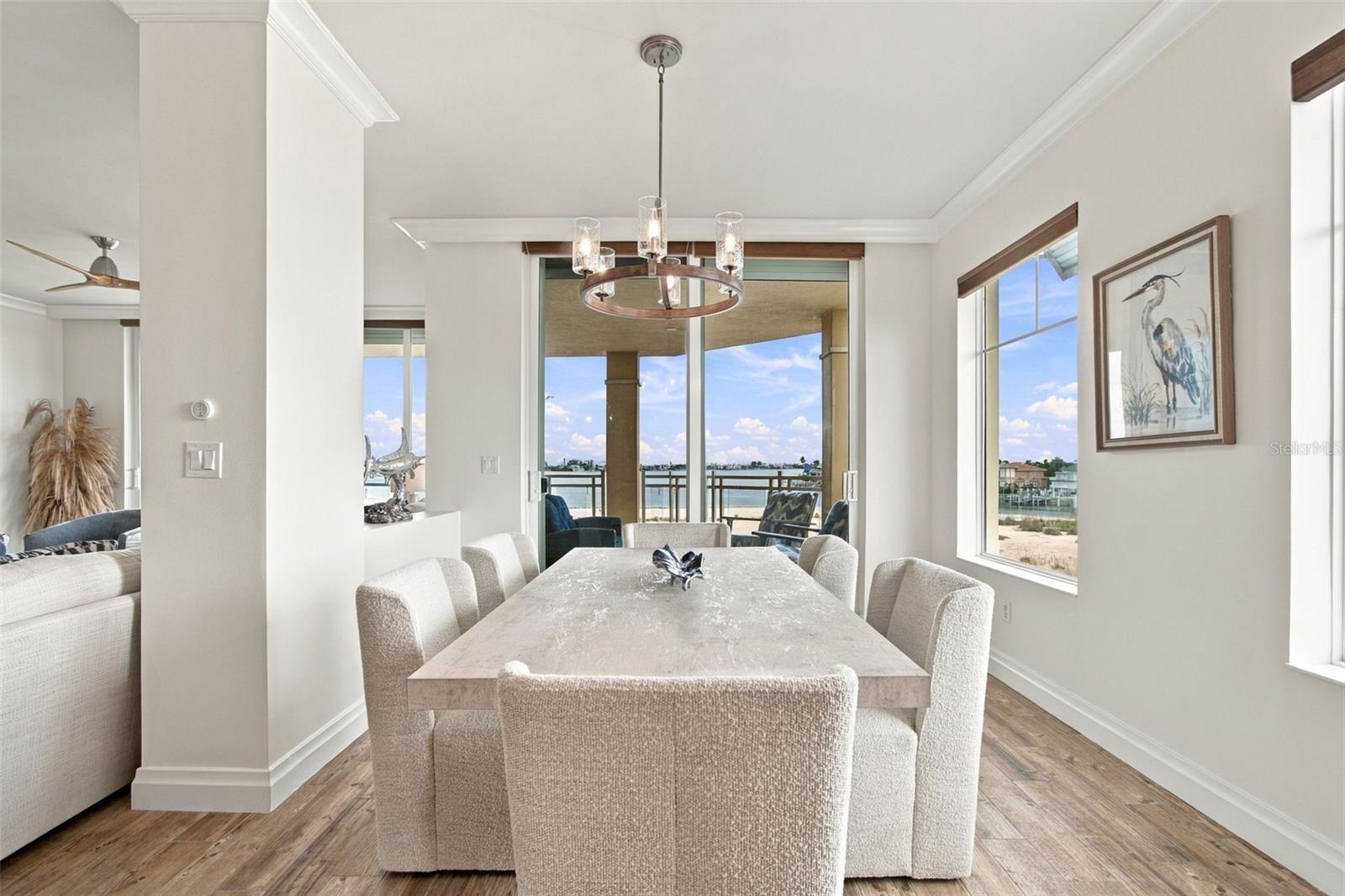 Dining room with a chandelier, upholstered chairs, and water views through large windows.