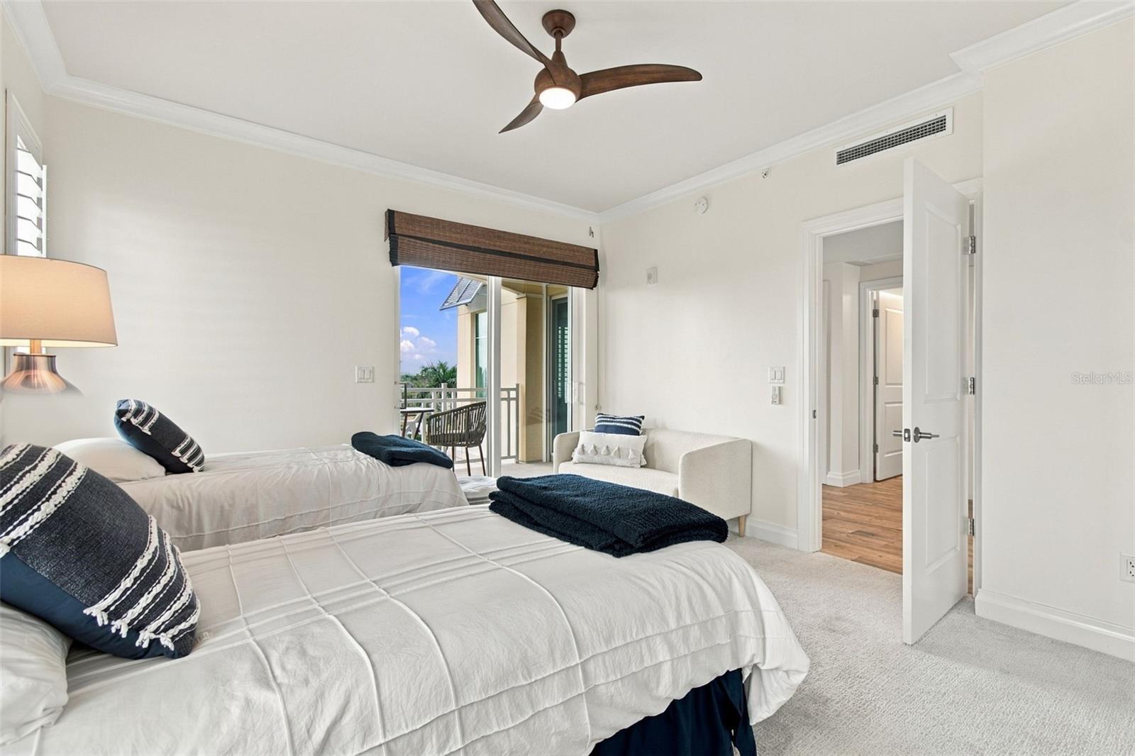 Furnished bedroom with two white beds, navy pillows, and a sliding door to the balcony.