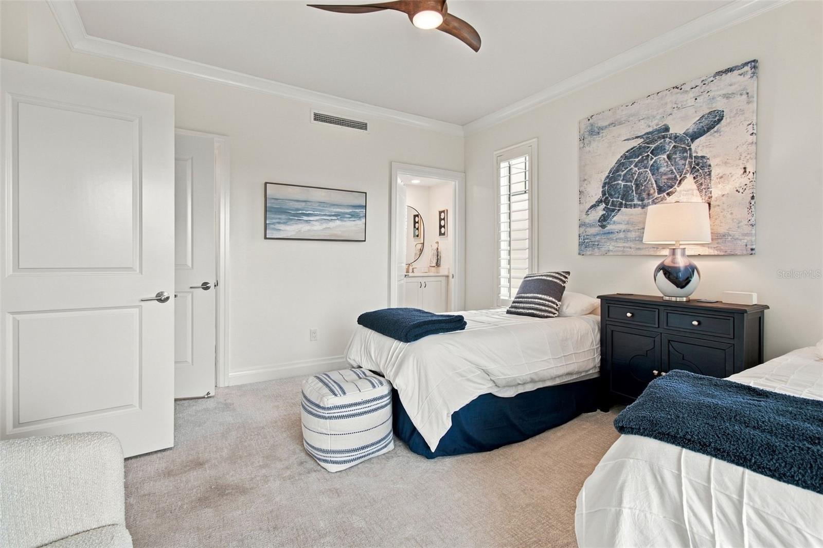 Furnished bedroom with twin beds, navy bedding, coastal artwork, and a dark nightstand.