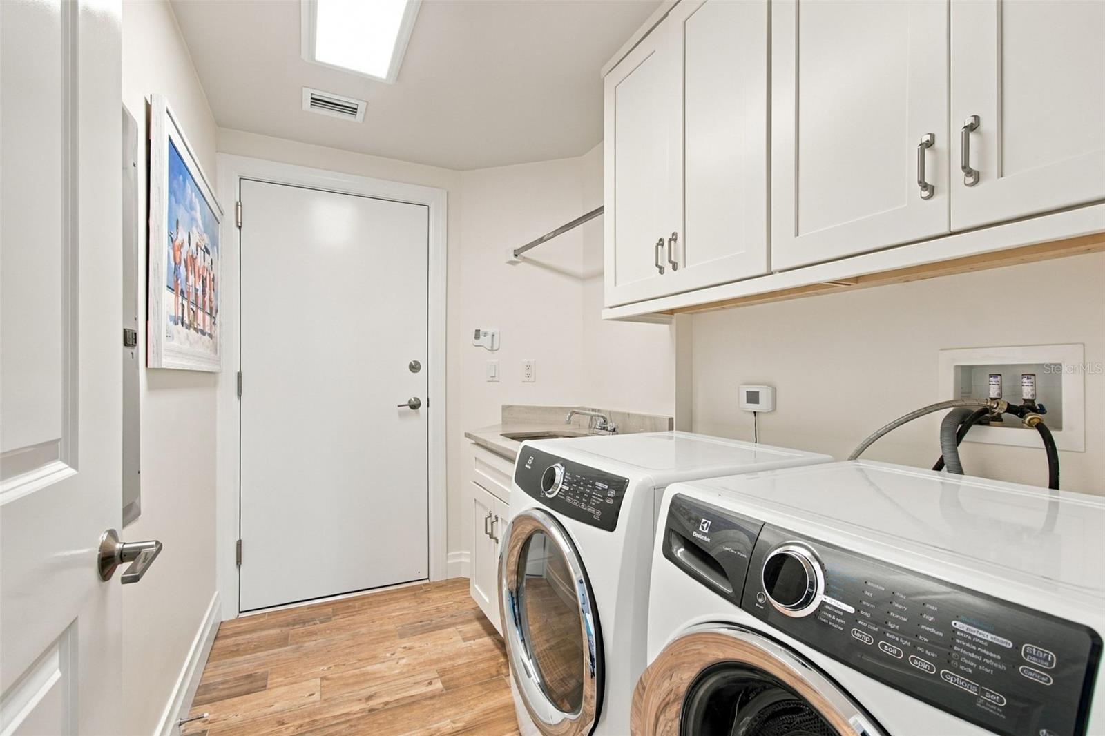 Laundry room with front-loading washer and dryer, white cabinets, and a utility sink.