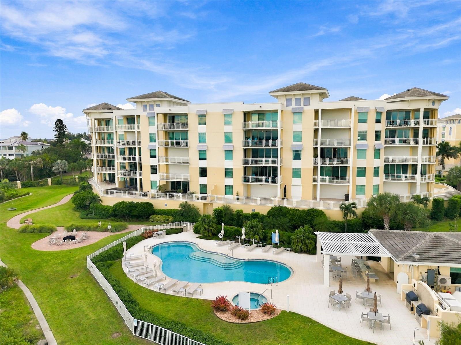 Condominium building with balconies overlooking a landscaped pool courtyard.