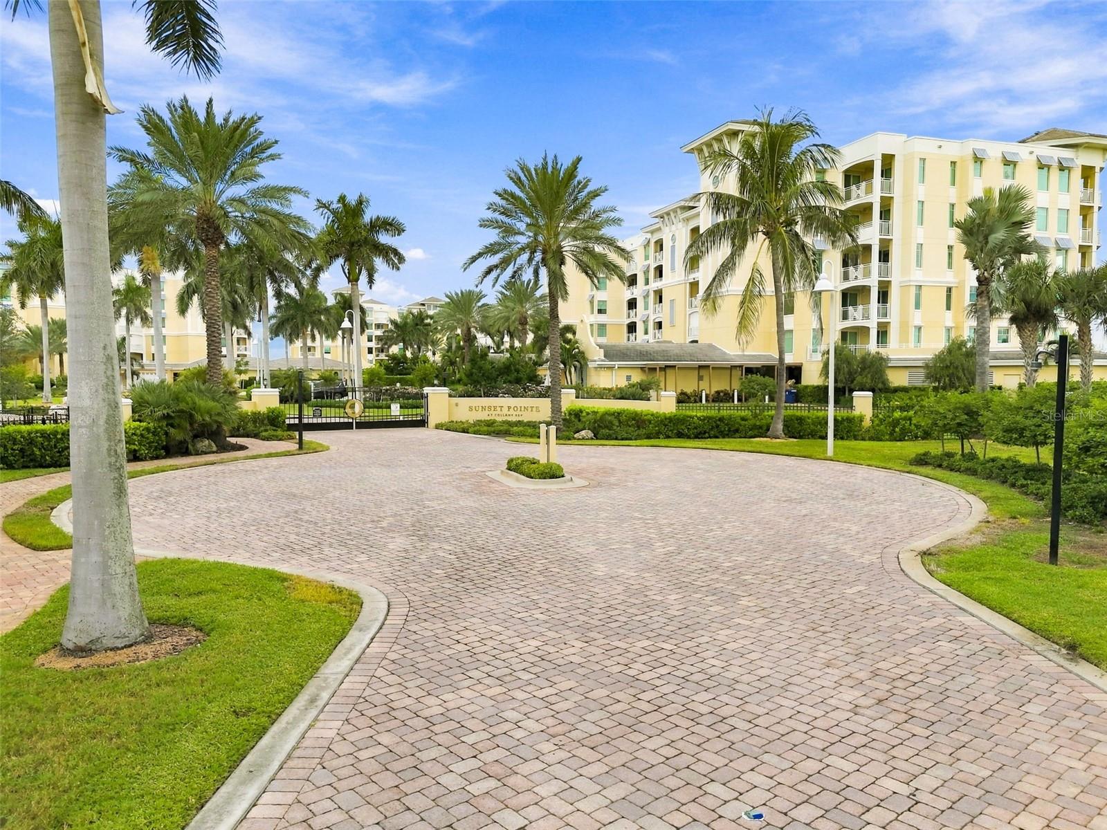 Sunset Pointe condominium entrance with palm trees, a gate, and a circular paver driveway.