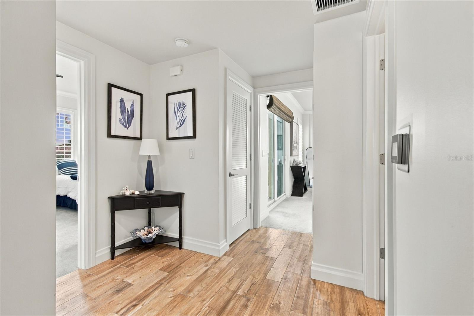 Condo hallway with wood-look flooring, framed botanical prints, and a dark console table.