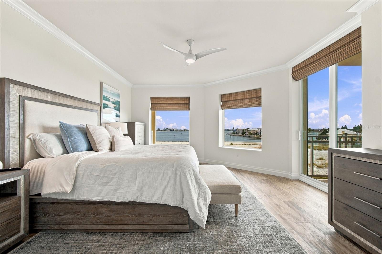 Bedroom with a large bed and water views through multiple windows and a glass balcony door.